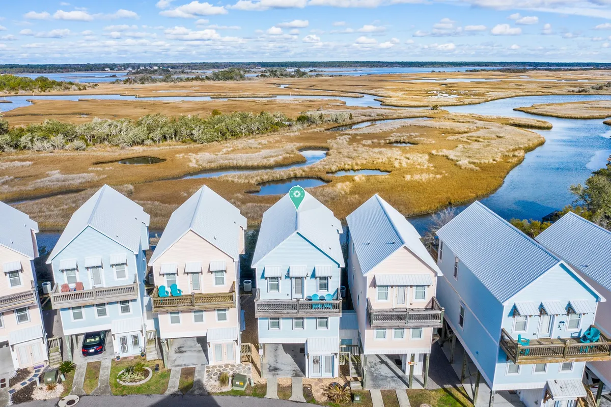 An exterior view showing colorful houses nestled along a marshland waterway. The scenery blends residential charm with natural beauty, evoking the sense of a vibrant, activity-filled community near both water and land attractions.