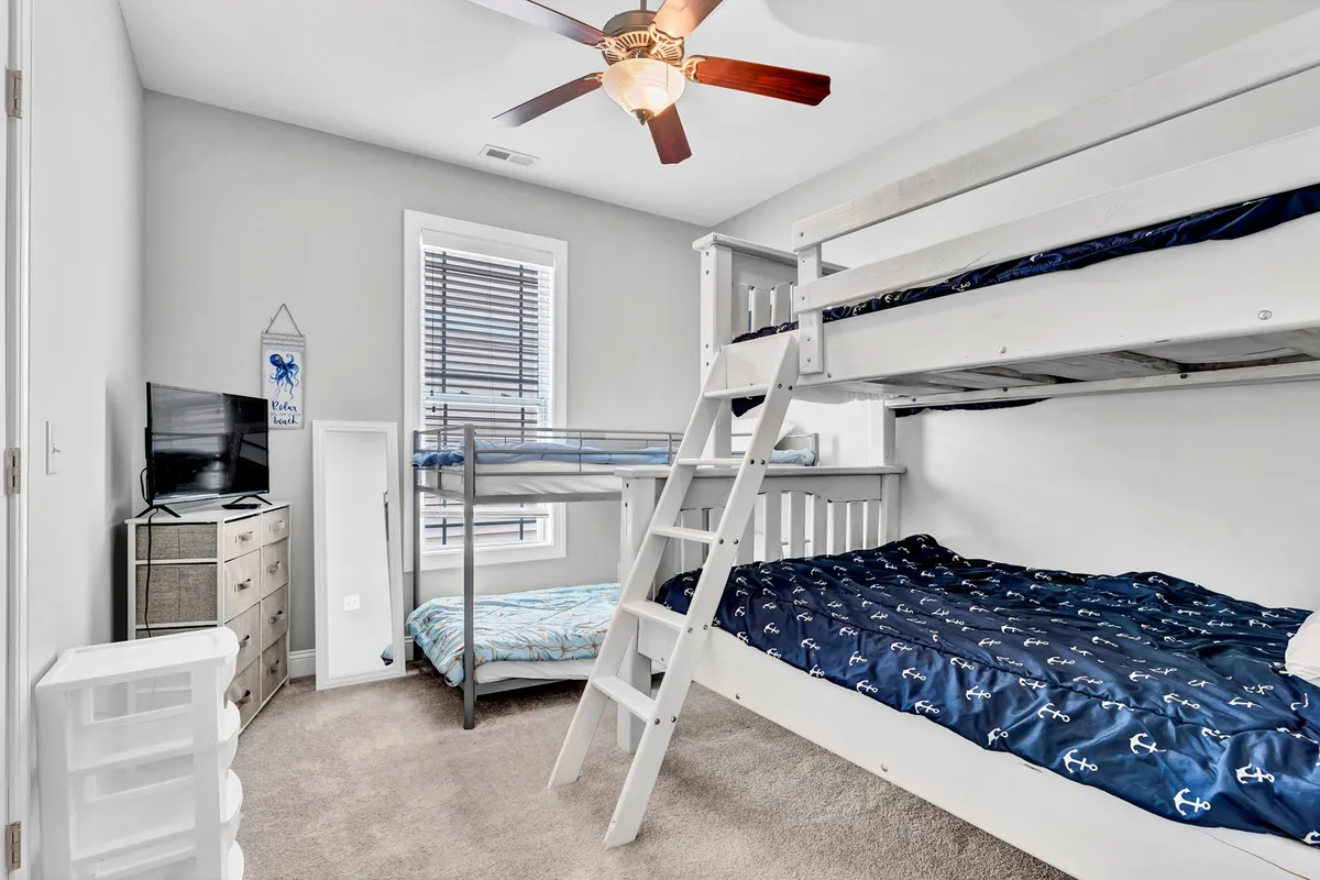 A cozy bunk room featuring neatly made bunk beds, a television, and a dresser. The space is tailored for children, with playful energy and comfort, making it ideal for kids to unwind, play, and bond.