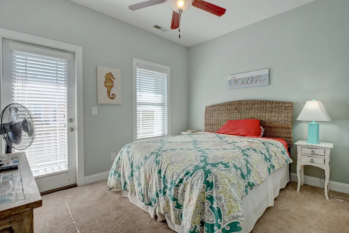 A cozy bedroom featuring a bed with colorful bedding, seahorse artwork above the headboard, and a nightstand with a lamp. Natural light streams in through the windows, creating a welcoming environment ideal for rest and relaxation.