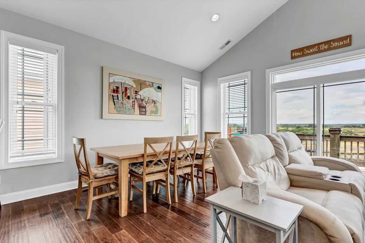A warmly lit dining area featuring a large table that seats eight, complemented by inviting décor and artwork on the wall. The space boasts large windows that frame beautiful views, creating an ideal spot for meals, conversation, and sunset watching.