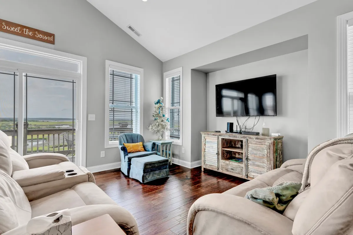 A cozy living room with comfortable seating, a television, a decorative wooden console, and expansive windows framing scenic sunset views. The space is perfect for unwinding after a day in the sun or hosting a movie night with friends and family.