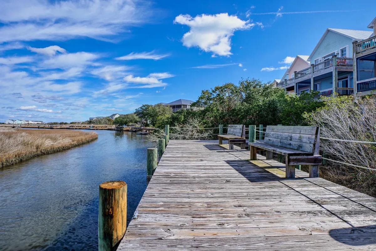 A tranquil wooden dock extends out over calm waters, surrounded by lush green vegetation. Benches on the dock invite relaxation or provide a spot for fishing, while the wide expanse of the waterway hints at opportunities for kayaking or paddleboarding.