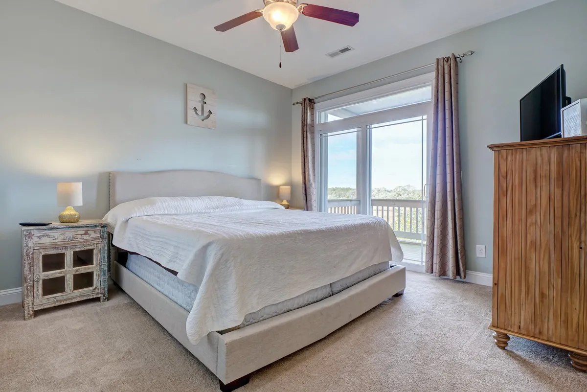 A serene bedroom with a comfortable bed, a nightstand topped with a lamp, a window letting in soft daylight, and a dresser. The overall feel is airy and peaceful, perfect for relaxation and restful sleep.