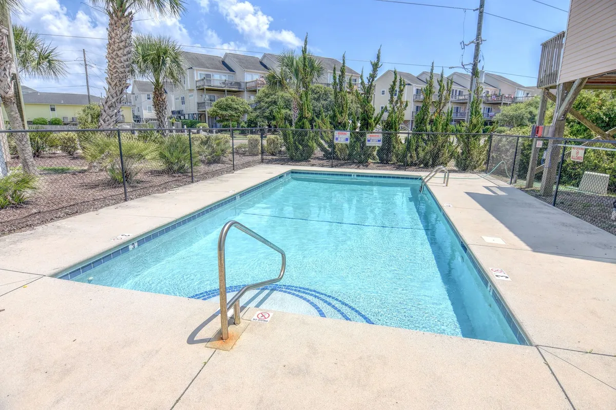 A bright and inviting scene of a sparkling swimming pool surrounded by palm trees and a secure fence. The water glistens under the sun, and the area is set up for relaxation and recreation, capturing the quintessential summer pool experience.