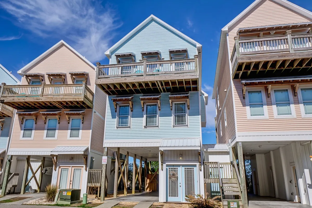 This image displays colorful exteriors of beach houses with balconies and inviting architectural details. The atmosphere is welcoming and hints at a community-oriented neighborhood very close to the shore, perfect for families heading out for a beach day.