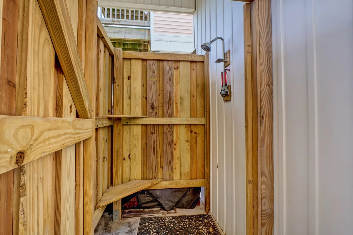 An inviting wooden outdoor shower enclosure with a bench seat, designed for rinsing off after a day on the sand. The setting feels refreshing and functional, perfect for families returning from beach play.