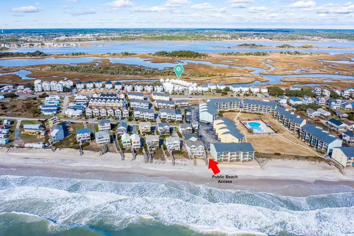 An elevated view showcasing dedicated beach access with a sandy shoreline, ocean waves, and a glimpse of the surrounding residential area and a nearby pool. The proximity of the beach, pool, and homes highlights the ease of enjoying both community and natural amenities.