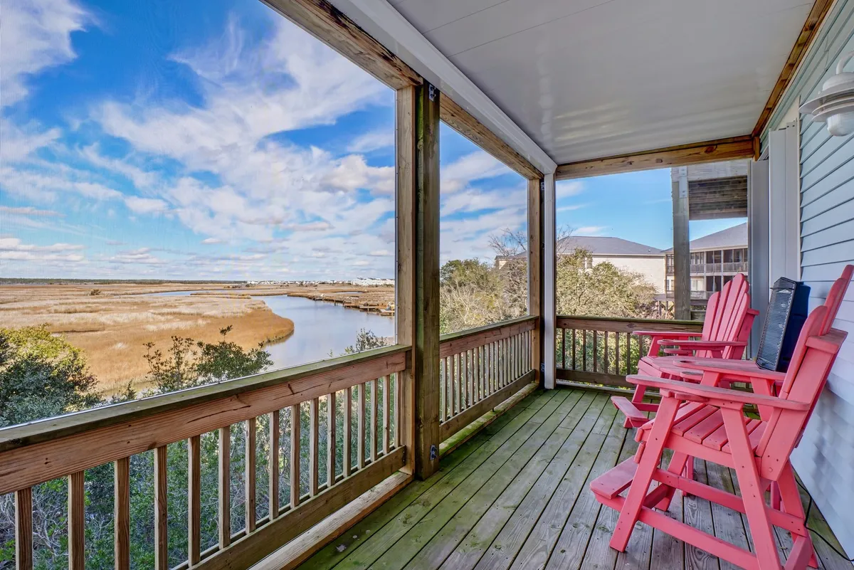Pink Adirondack chairs are arranged on a wooden deck, facing a tranquil river view, framed by a simple wooden railing. The tranquil mood and waterway vista evoke the perfect spot for evening drinks or conversations as the sun sets.