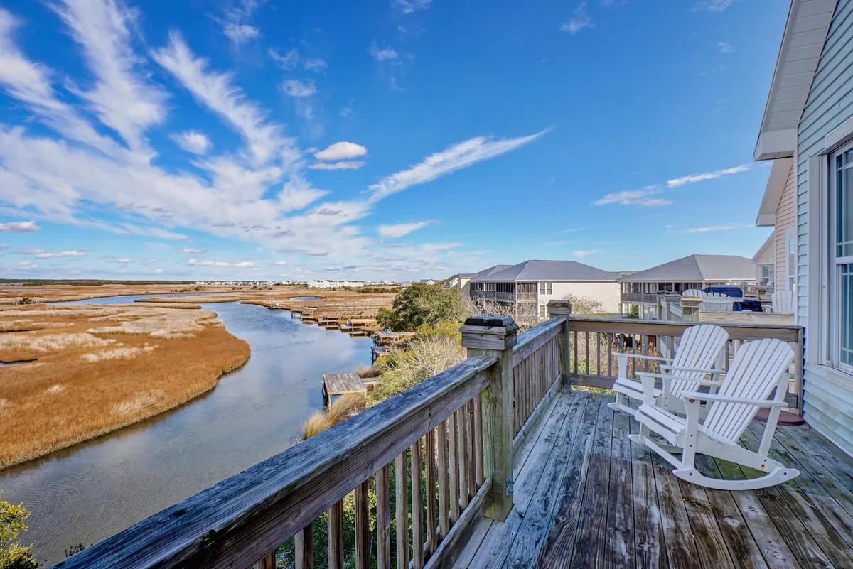 A serene deck with white chairs overlooks a sweeping view of the river and marshland, with the colorful sky suggesting the approach of sunset. The peaceful setting is perfect for relaxing outdoors while enjoying the natural beauty of the Intracoastal Waterway.