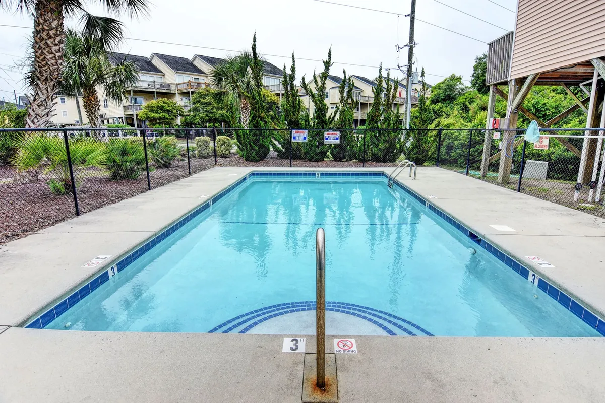 A sparkling swimming pool sits at the center of a fenced area, surrounded by palm trees, creating an inviting, resort-like atmosphere for relaxation and family fun during the summer months.
